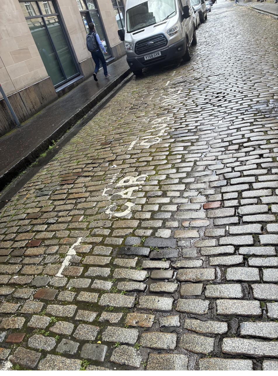 Very faded white parking bay markings on Edinburgh cobblestone street with barely legible text