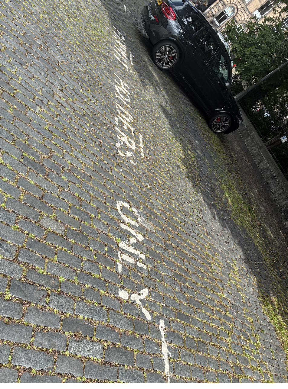 Faded white permit holders only text painted on Edinburgh cobblestone road surface