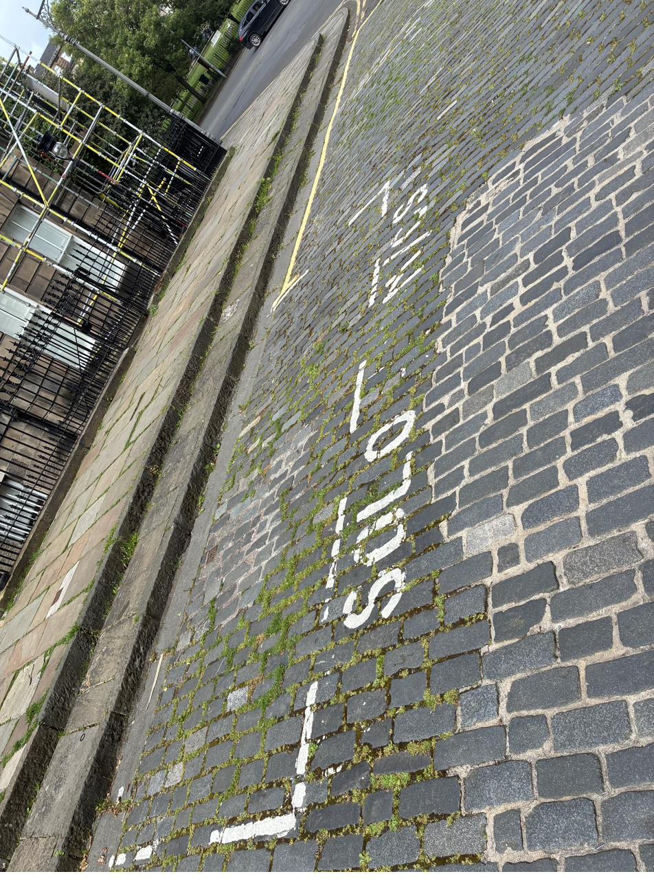 Solo motorcycle parking bay markings on Edinburgh cobblestone street with faded white text and yellow line visible